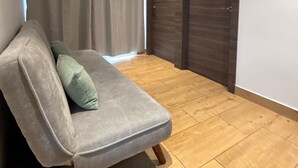 Een grijze bank met een groen kussen in een kamer met houten vloeren en een donkerhouten deur.