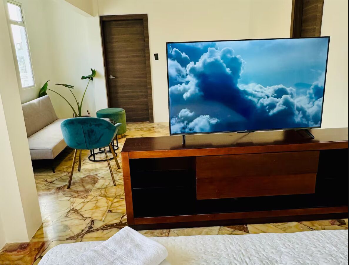 A room with a TV on a wooden stand, a sofa, a teal chair, and a plant.
