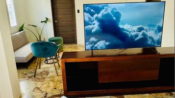 A room with a TV on a wooden stand, a sofa, a teal chair, and a plant.