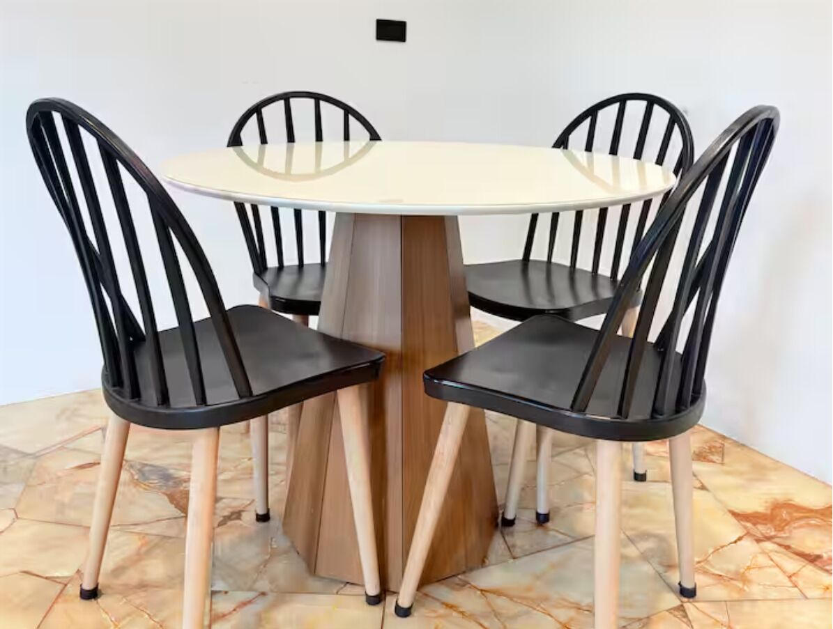 Une table ronde avec un piétement en bois, entourée de quatre chaises noires aux pieds en bois.