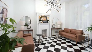 A modern living room with a checkered floor, a brown sofa, a fireplace, and a chandelier. - The Suites | Downtown Montreal (Montreal)