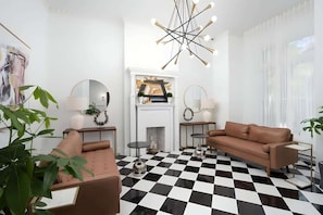 Un salon moderne avec un sol à carreaux, un canapé marron, une cheminée et un lustre.