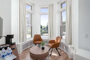 Une pièce d’angle avec deux fauteuils marron, une table ronde en bois et une vue sur la rue grâce à de grandes fenêtres.