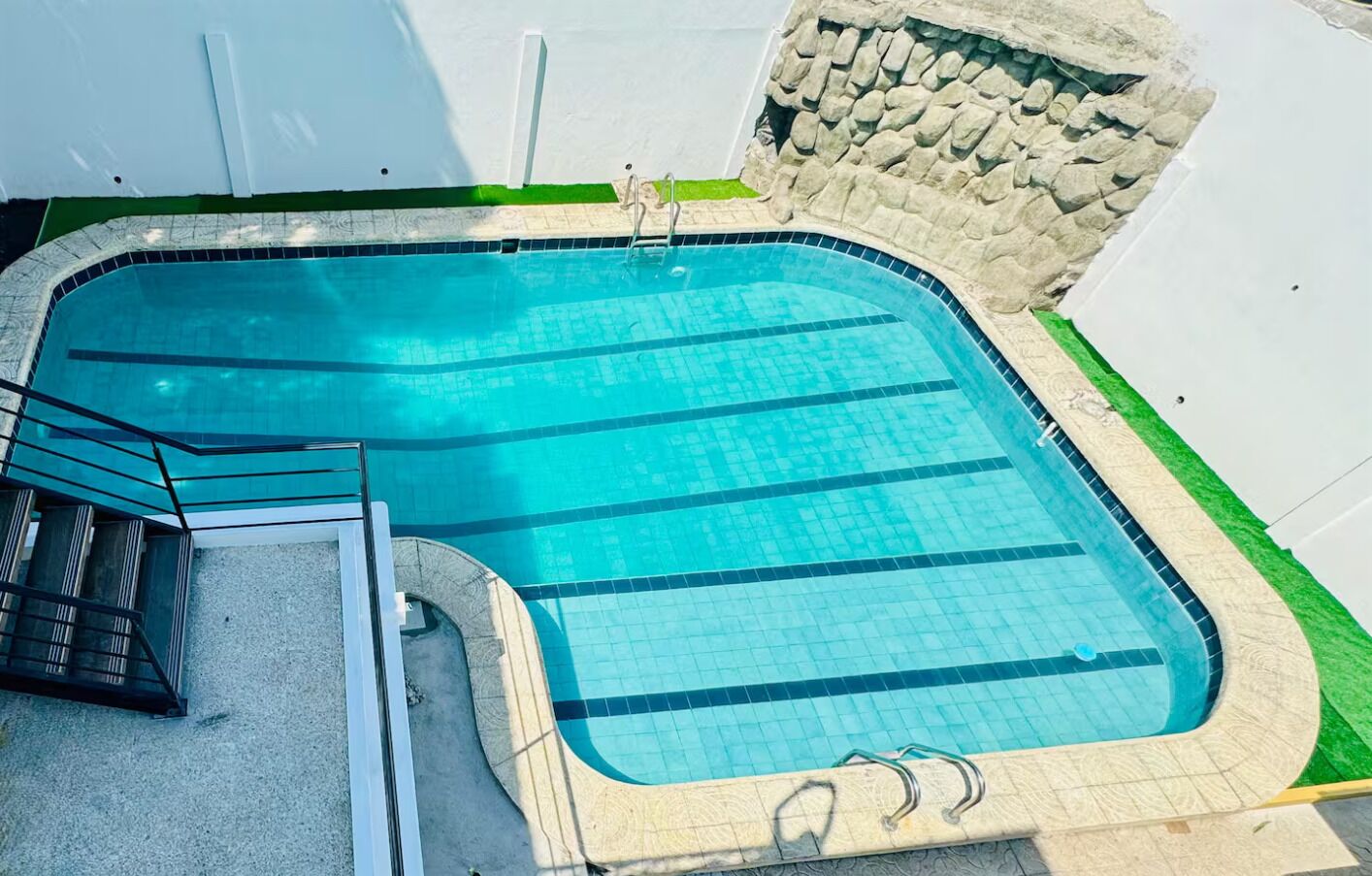 Ein Schwimmbecken mit Steinmauer, Metallleiter und einer kleinen Rasenfläche.