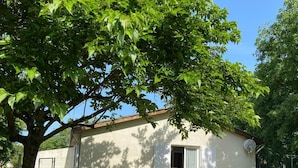 Una casa con un porche cubierto, una mesa con sillas y un árbol grande que da sombra.