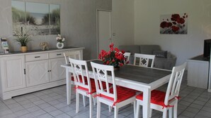 Un comedor con una mesa y sillas blancas, una planta en maceta y un cuadro en la pared.