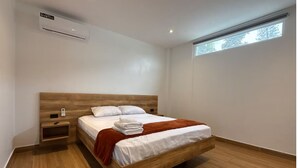 A modern bedroom with a wooden bed, a nightstand, an air conditioning unit, and a window. - Suite 09 • Private Suite • Boutique Mansion (Guayaquil)