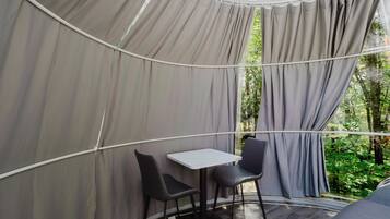 Une structure en forme de tente, avec une table et des chaises à l’intérieur, entourée de rideaux et offrant une vue sur la verdure.