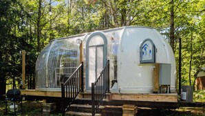 Une maison mobile en forme de dôme, dotée d’un porche couvert et d’un escalier menant à l’entrée.