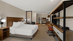 Hotellihuone, jossa on sänky, yöpöydät, työpöytä tuolilla, pieni keittiö ja televisio.