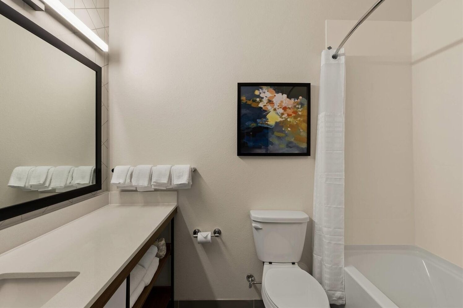 Une salle de bain équipée de toilettes, d’un lavabo et d’une douche. On y trouve un porte-serviettes avec des serviettes et un tableau accroché au mur.