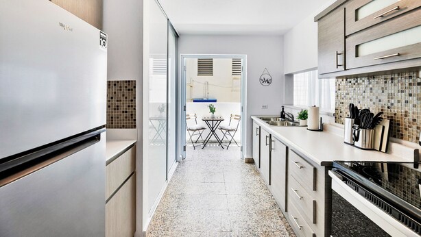 A modern kitchen with a refrigerator, cabinets, a tiled backsplash, and a dining area with a table and chairs. - 3BR Near Restaurants & Nightlife Sleeps 7 (San Juan)