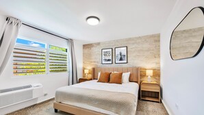 A hotel room with a bed, two nightstands, a window with blinds, a wall-mounted mirror, and two framed pictures. - 3BR Near Restaurants & Nightlife Sleeps 7 (San Juan)