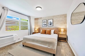 A hotel room with a bed, two nightstands, a window with blinds, a wall-mounted mirror, and two framed pictures. - 3BR Near Restaurants & Nightlife Sleeps 7 (San Juan)