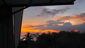 Vista desde un balcón con piscina, con atardecer y zona boscosa.