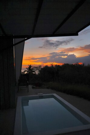 Blick vom Balkon auf einen Pool, bei Sonnenuntergang und mit Blick auf ein bewaldetes Gebiet.