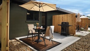 Un patio al aire libre con una mesa, sillas, una parrilla y una cerca de madera.