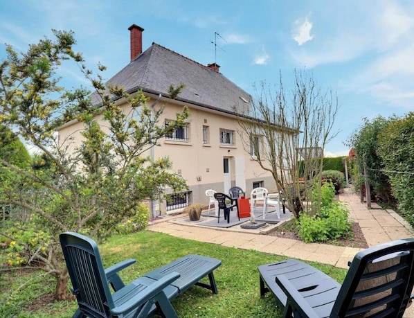 A two-story house with a garden patio, outdoor seating, and a visible chimney.