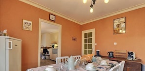 A dining area with a table set for two, a refrigerator, and a kitchen visible in the background.