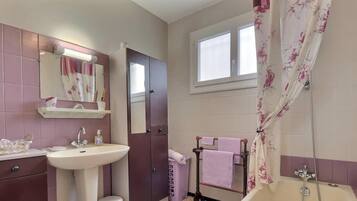 A bathroom with a sink, mirror, vanity, toilet, shower, and a window.