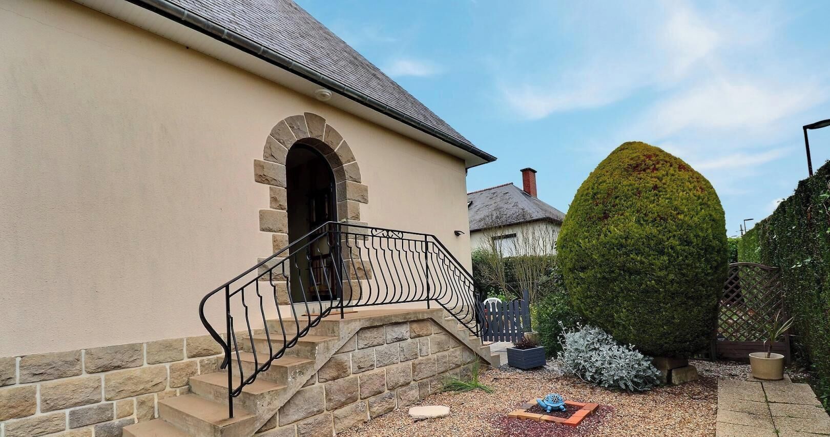 A building with a stone staircase, a metal railing, and a well-maintained garden with various plants and a small decorative item.