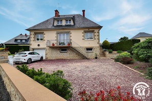A two-story house with a stone facade, a balcony, and a gravel driveway.