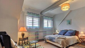 A bedroom with a bed, two bedside tables, a chair, a lamp, and a window with curtains.