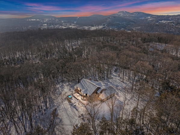 A snow-covered landscape with a cabin featuring a large deck and a hot tub.