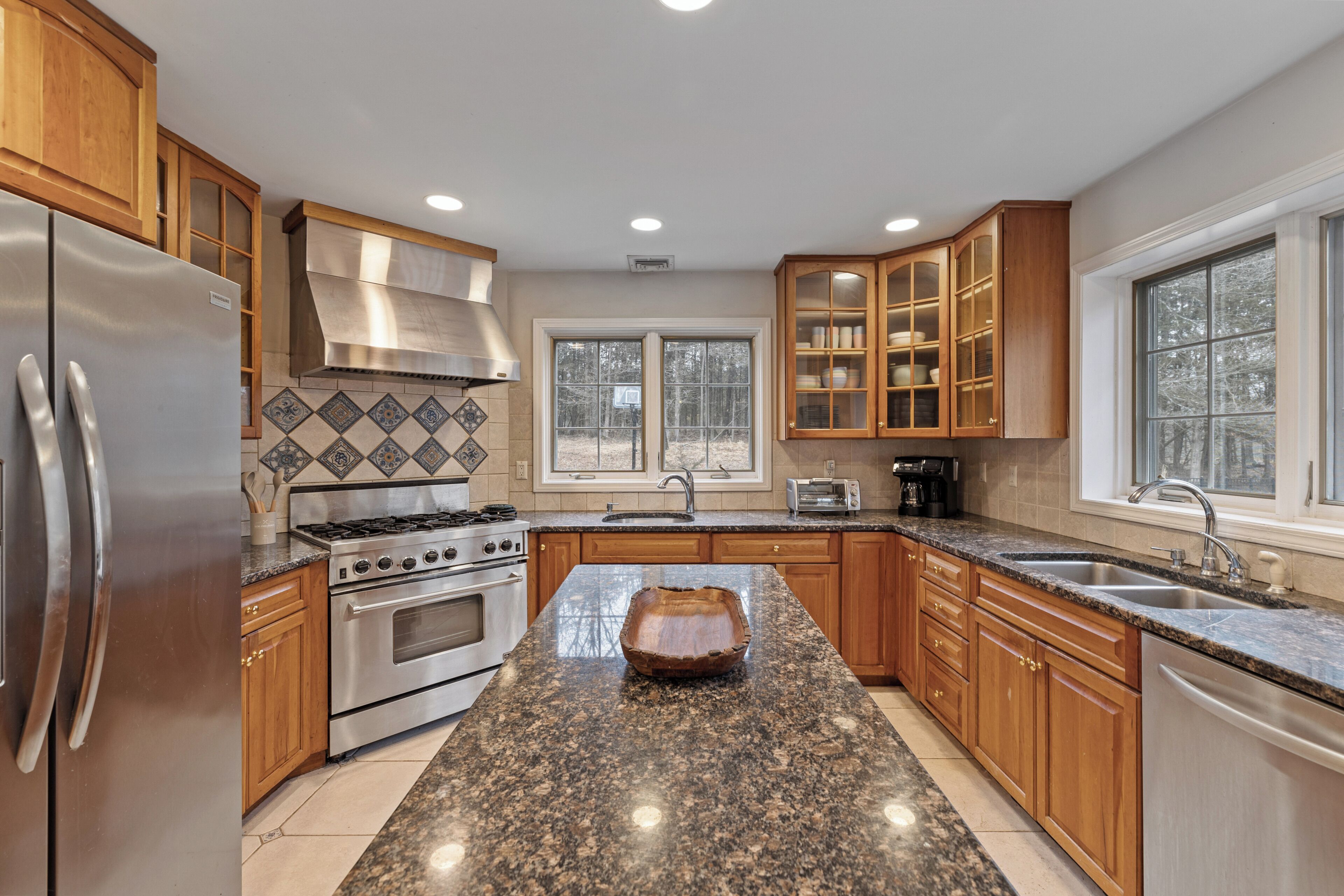 A kitchen with granite countertops, stainless steel appliances, wooden cabinets, and a large window.