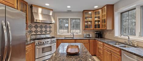 A kitchen with granite countertops, stainless steel appliances, wooden cabinets, and a large window.