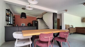 A modern dining area with a wooden table and pink chairs, a kitchen in the background, and a staircase leading to another level. - Luxury house in the heart of the Luberon (Apt)