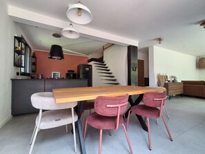 Ein moderner Essbereich mit einem Holztisch und rosa Stühlen, im Hintergrund eine Küche und eine Treppe, die zu einer weiteren Ebene führt.