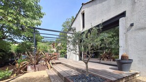 A modern outdoor deck with a wooden floor, surrounded by plants and a metal pergola. - Luxury house in the heart of the Luberon (Apt)