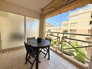 A balcony with a table and chairs, a statue, and a view of buildings and greenery. - Golfe Juan - 4 people - Swimming pool - Parking (Vallauris)