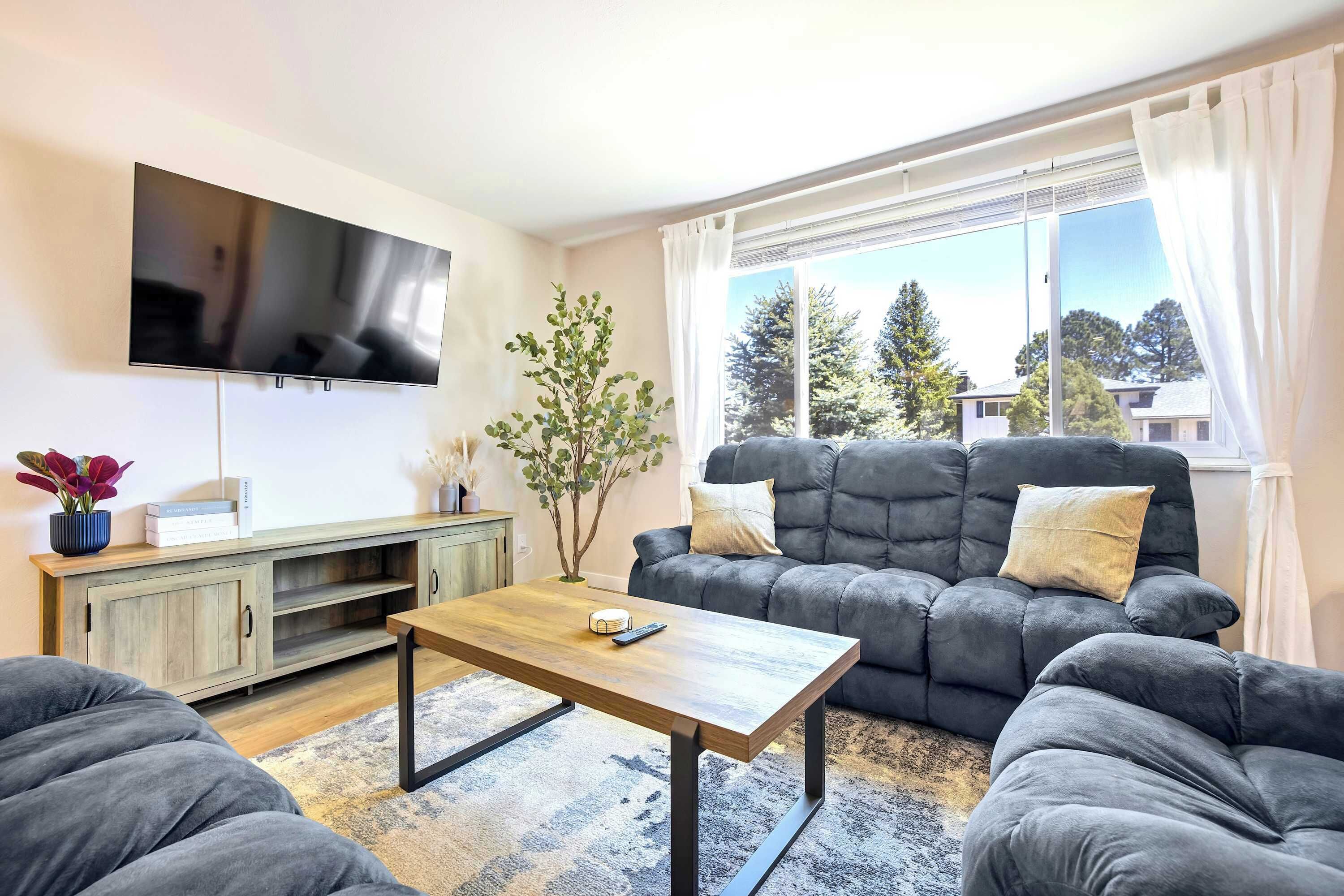 Un salon comprenant un canapé, une table basse, un téléviseur fixé au mur et une fenêtre avec des rideaux.