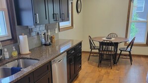Una cucina con mobili scuri, un piano di lavoro in granito, una lavastoviglie e un'area pranzo con tavolo e sedie in legno.