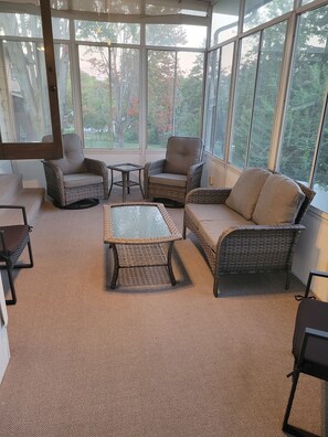 A sunroom with wicker furniture, a glass coffee table, and a view of trees. - Spacious 4-bed/3-bath house in Iowa City - 1.2 miles from Kinnick and UIHC (Iowa City)
