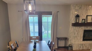 Una sala da pranzo con un grande tavolo in legno, sedie, un lampadario e vista attraverso una porta vetrata.