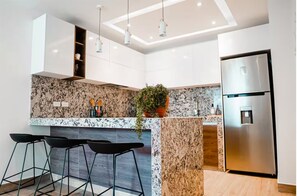 Eine moderne Küche mit Granitarbeitsplatte, Edelstahlgeräten und schwarzen Barhocker.