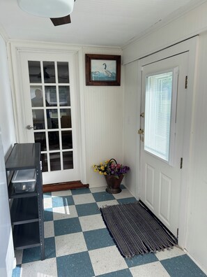 A room with a checkered floor, a door with a window, a framed picture on the wall, and a metal container with flowers. - Completely revamped Eastern Shore home (Onley)