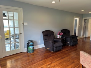 A spacious living area with hardwood flooring, two black armchairs, a small table with a vase of flowers, and a door leading to a balcony. - Completely revamped Eastern Shore home (Onley)