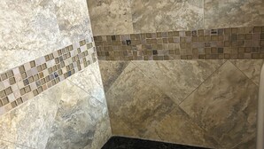Ein Badezimmer mit Marmorfliesen, einer schwarzen Arbeitsplatte und einer Bordüre aus Mosaikfliesen.