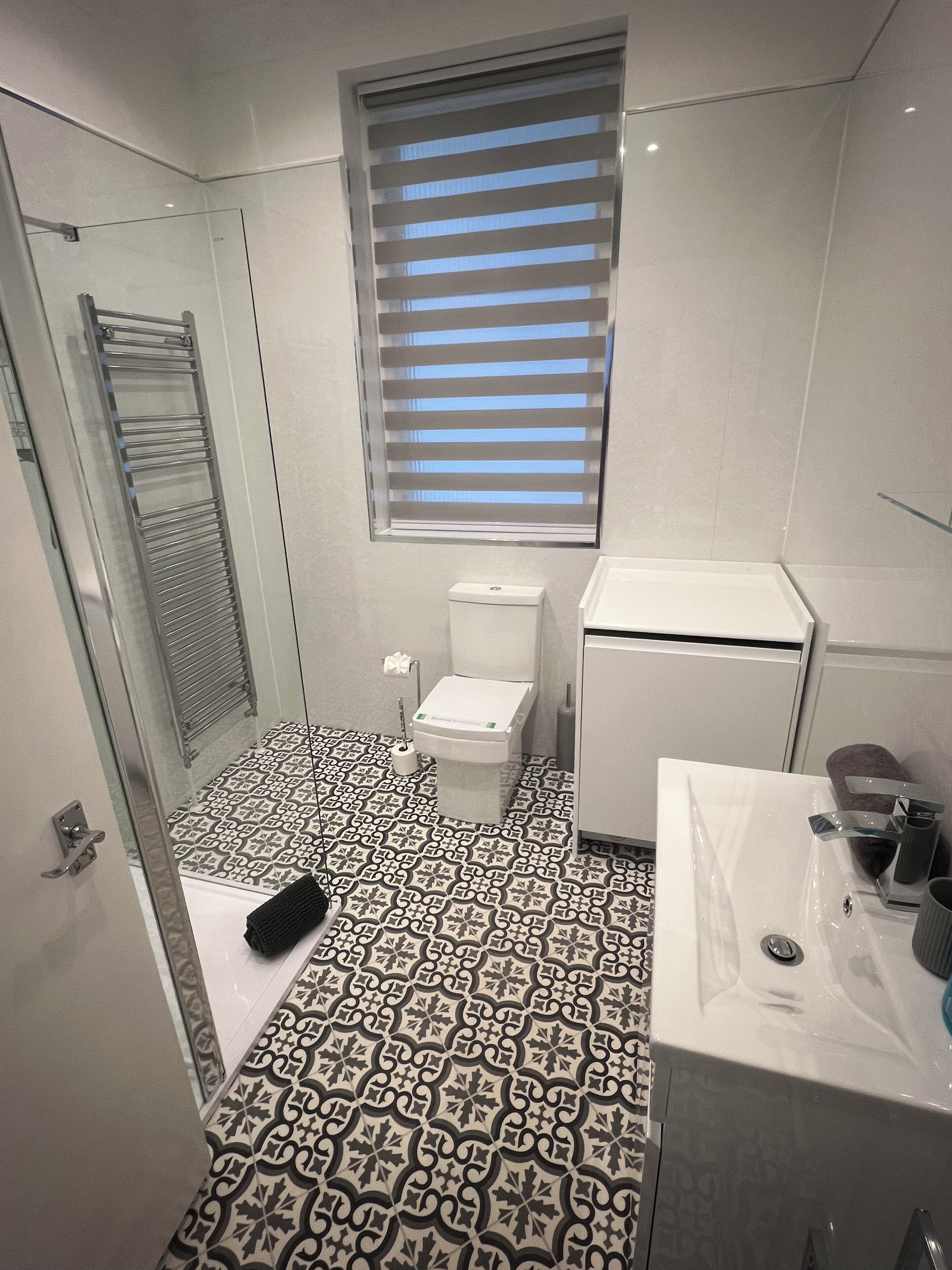 A bathroom with a patterned floor, a toilet, a sink, and a window with blinds.