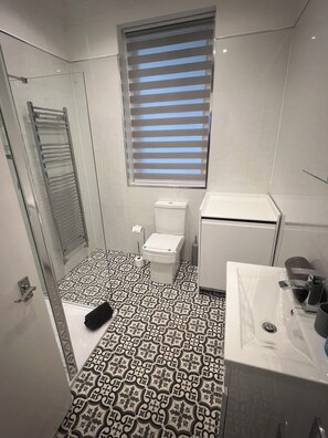 A bathroom with a patterned floor, a toilet, a sink, and a window with blinds. - 253
Stylish Coastal Retreat ground floor  1507sqf (Lytham St Annes)