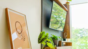 Ein Zimmer mit an der Holzwand montiertem Fernseher, einem gerahmten Kunstwerk und einer Topfpflanze.