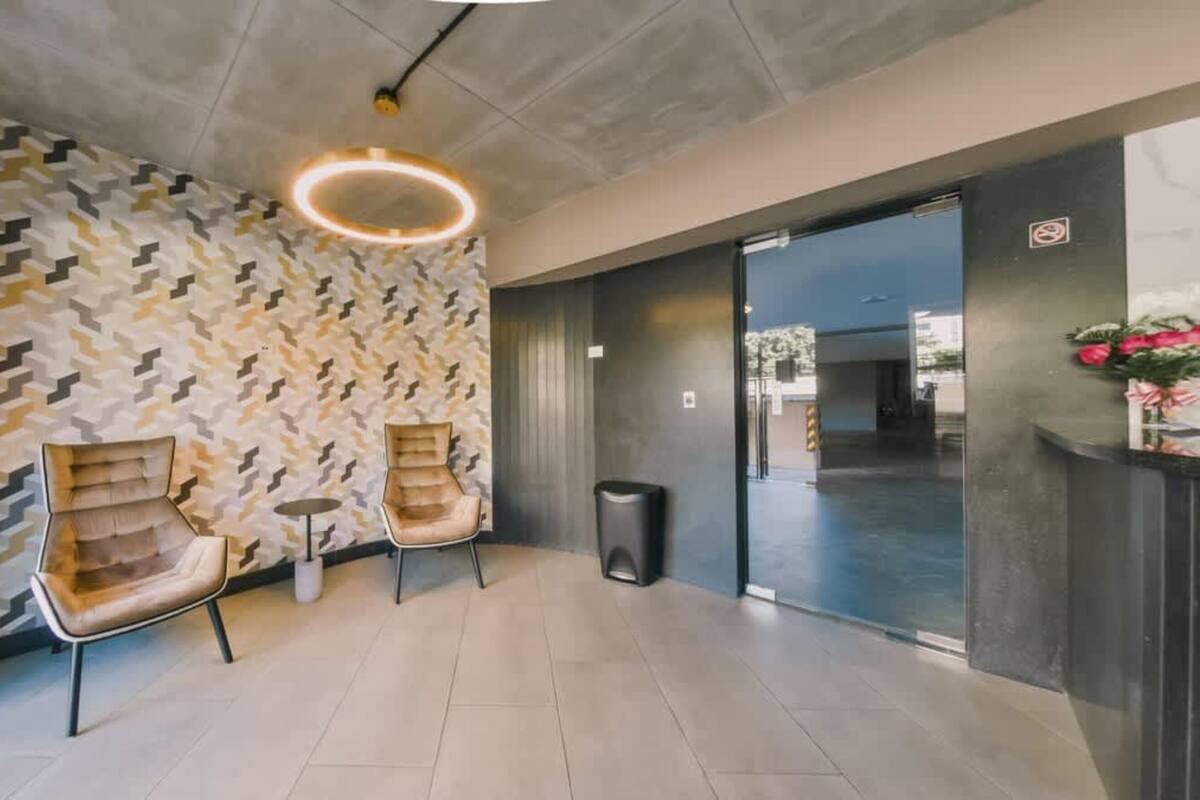 Eine moderne Lobby mit Wandmustern, zwei Ledersessel, ein Mülleimer und ein Empfangstisch mit Blumenvase.