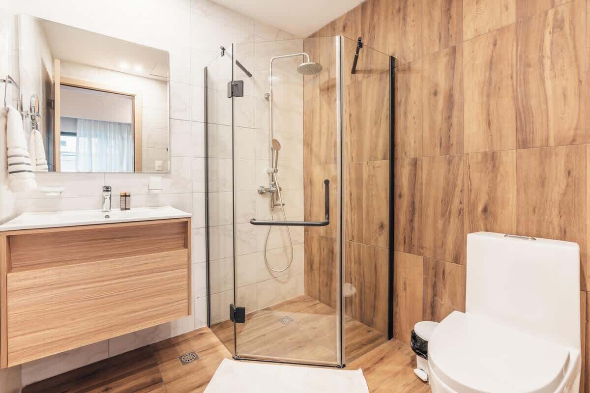 A modern bathroom with a glass-enclosed shower, a wooden vanity, and a white toilet.