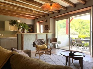 A cozy living area with a sofa, a wicker chair, a small table, and a view of the outdoors through a sliding glass door.