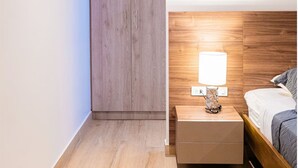 A bedroom with a wooden headboard, a bedside table with a lamp, and a bed with a gray blanket. - 07 Luxury Apartment Los Angeles style, brand new (Guayaquil)