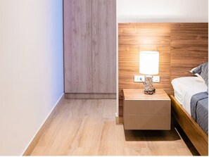 Une chambre à coucher avec une tête de lit en bois, une table de chevet avec une lampe et un lit recouvert d’une couverture grise.